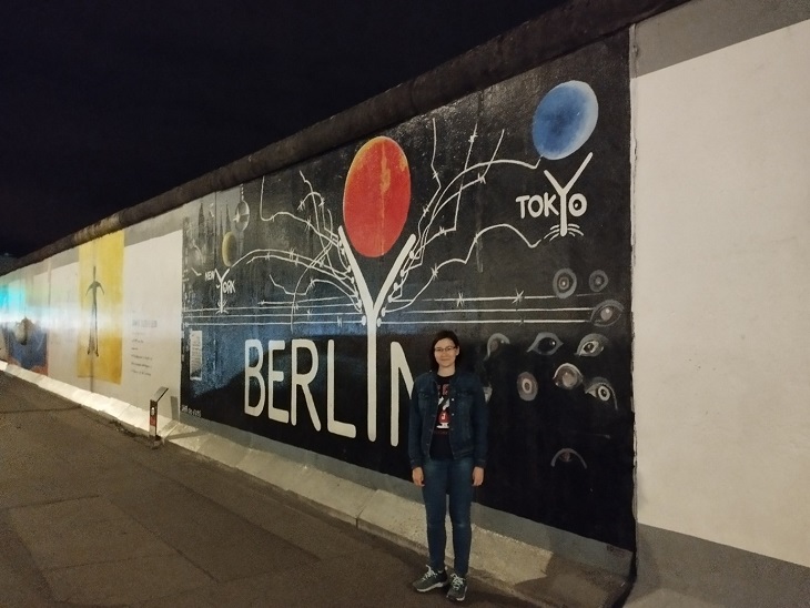 fiatal lány fekete alapon fehér és színes berlini falfestmény előtt áll