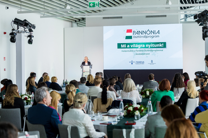 Egy teremben a Tempus Közalapítvány elnökasszonya mond köszöntőbeszédet a a hallgatóságnak