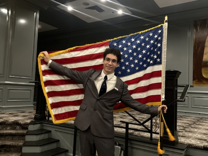 Pannónia Ösztöndíjas diák Vasali Dávid öltönyben amerikai zászlóval a kezében mosolyog a kamerába